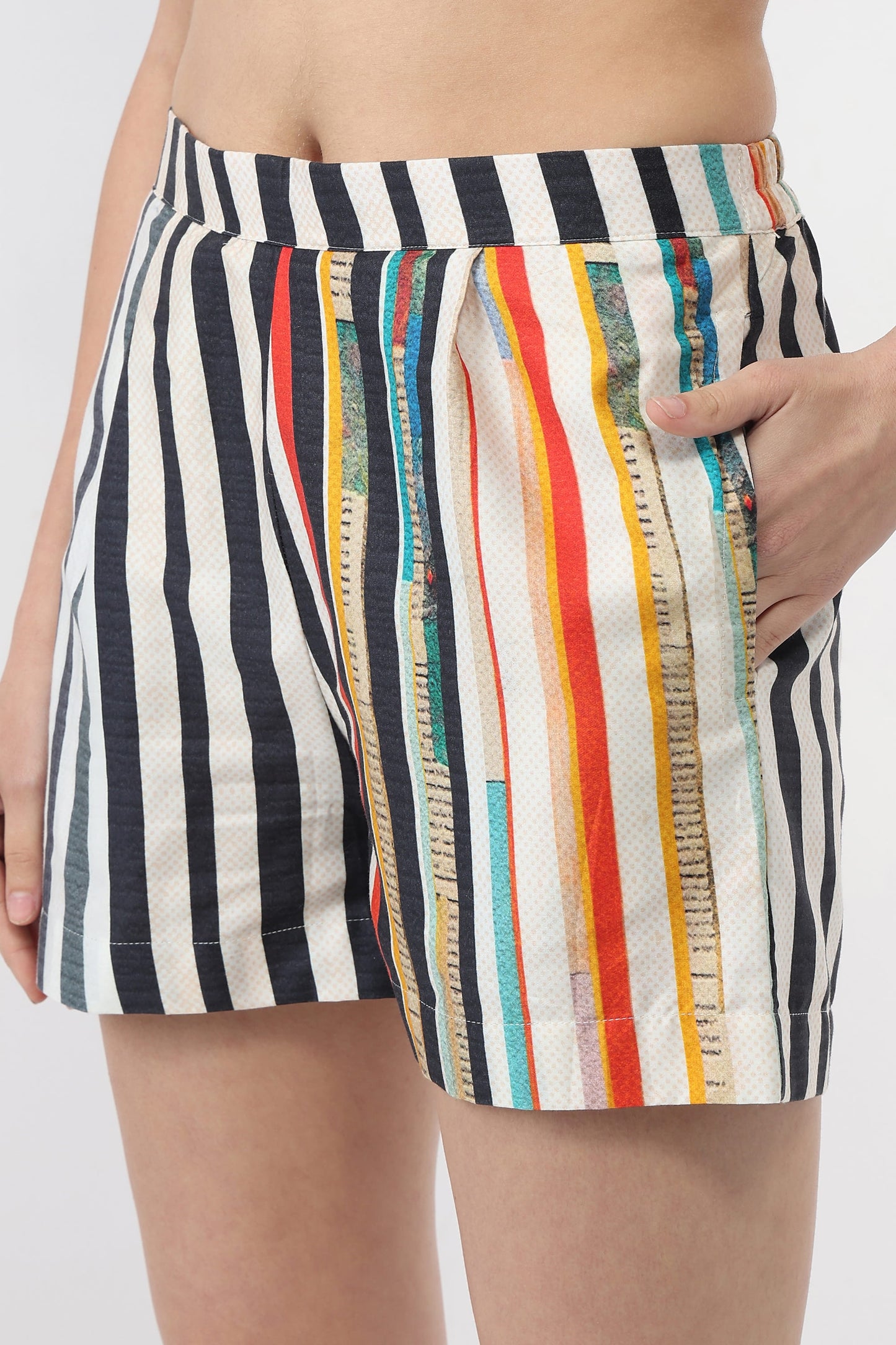A close-up of a person wearing striped shorts with vertical black, white, orange, red, yellow, and blue stripes, showing a hand in the pocket.