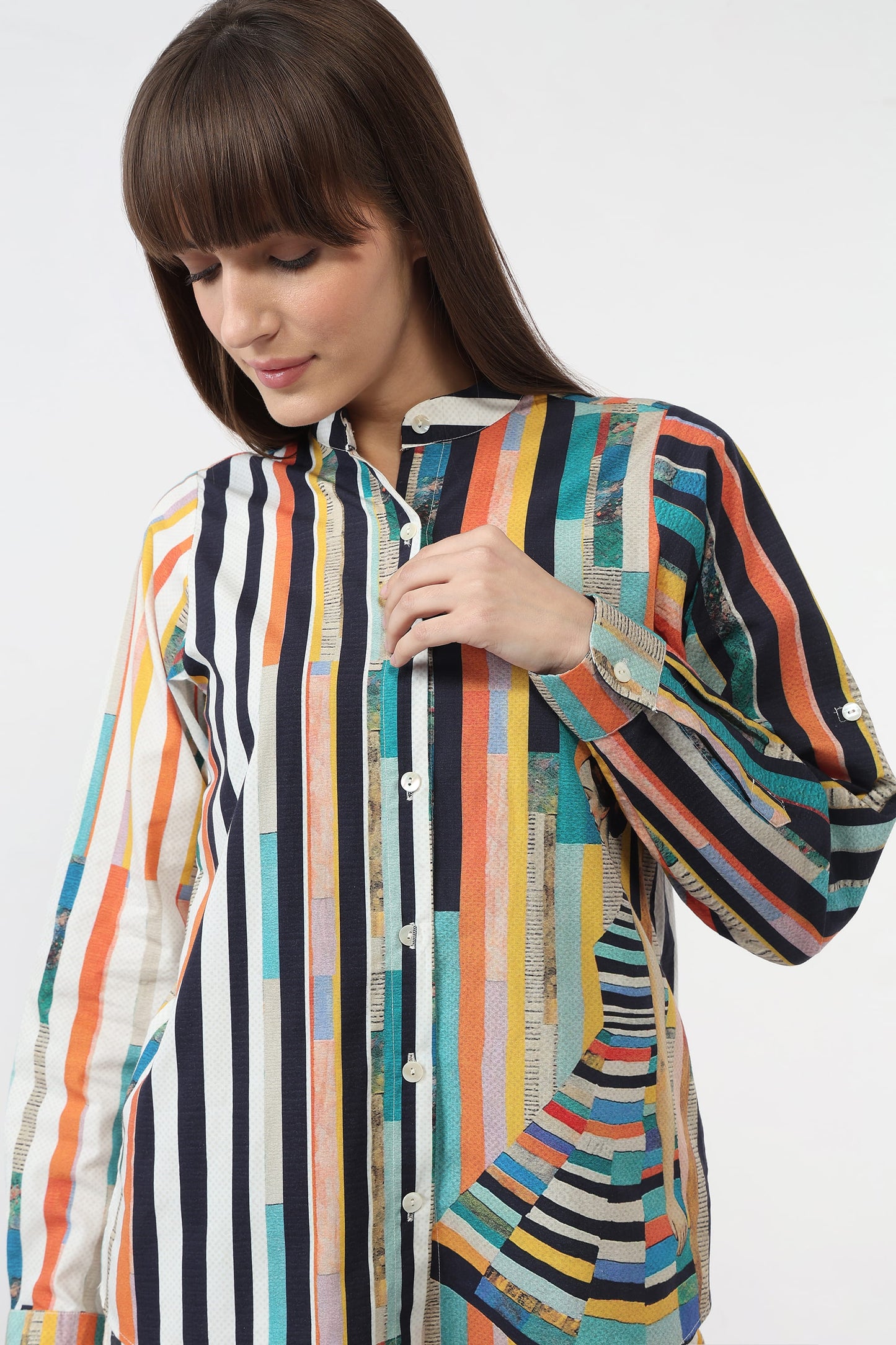 A woman wearing a long-sleeve button-up shirt with a vibrant multicolor vertical stripe pattern, featuring black, orange, teal, yellow, and white stripes.