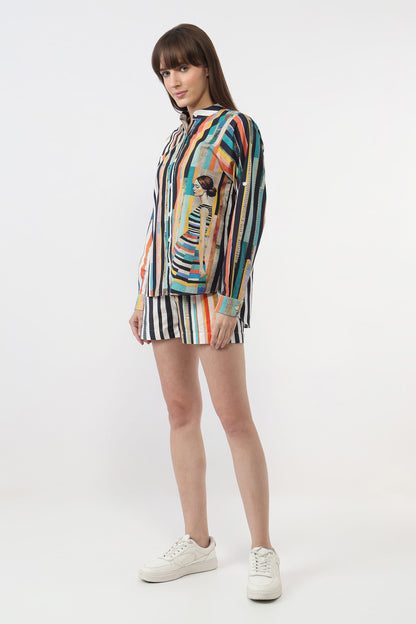 A woman modeling a colorful striped long-sleeve top and matching striped shorts with a central graphic print, paired with white sneakers, against a plain white studio background.