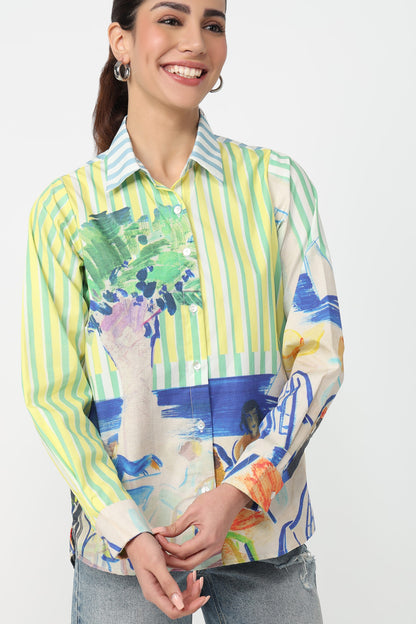 A woman wearing a long-sleeve button-up shirt with vertical lime green and white stripes on the upper body, transitioning into a multicolor abstract print with blue, green, orange, and white elements. The shirt has a light blue and white striped collar.