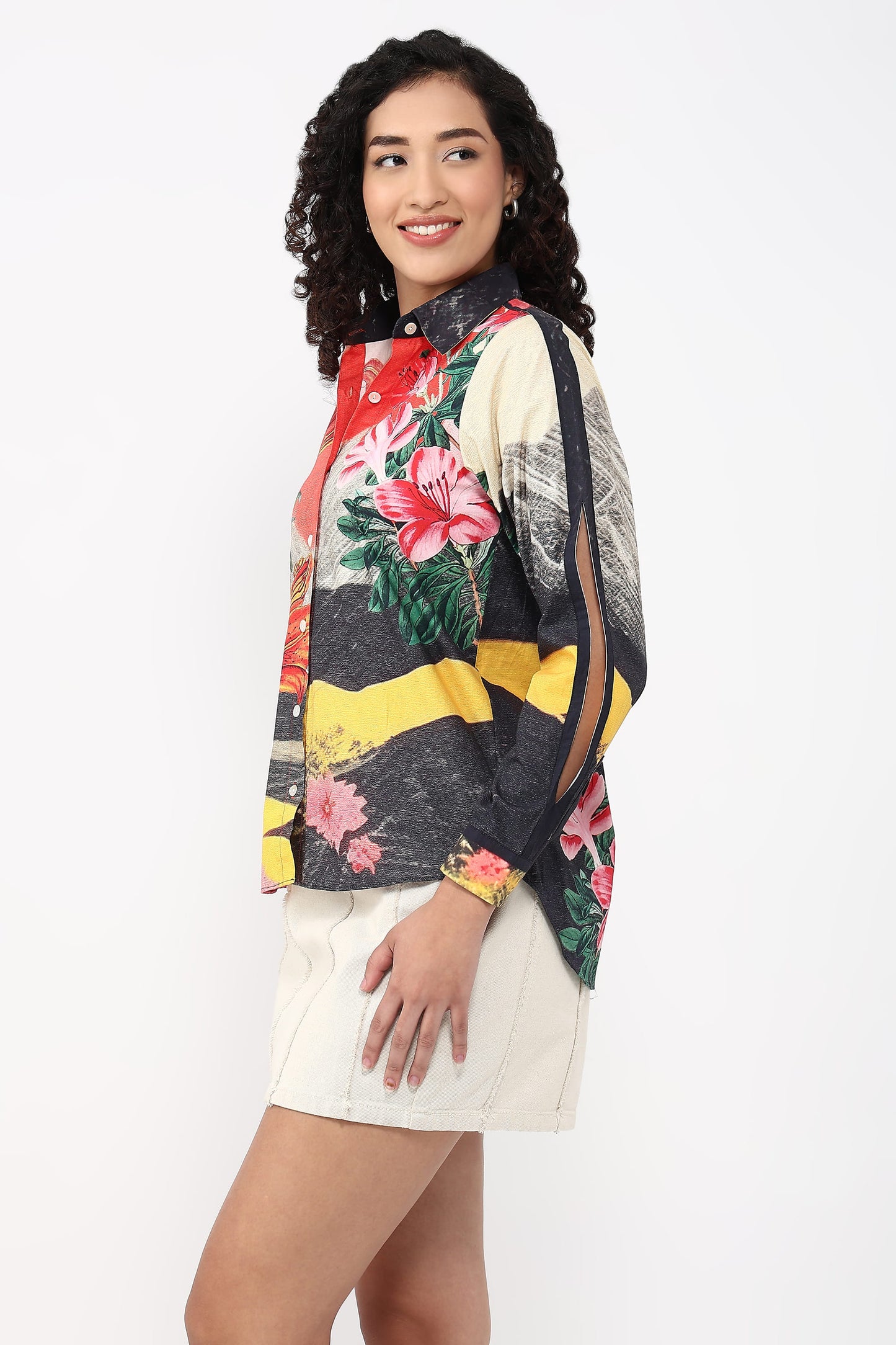 A woman modeling a long-sleeve blouse with a bold multicolor floral and abstract print, paired with off-white shorts, against a plain white studio background.