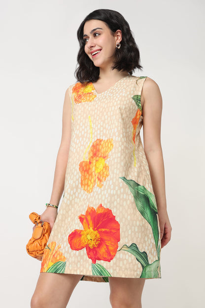 A woman wearing a sleeveless beige mini dress with a white polka dot pattern and large orange and red hibiscus floral prints, holding a textured orange clutch bag against a plain light grey background.