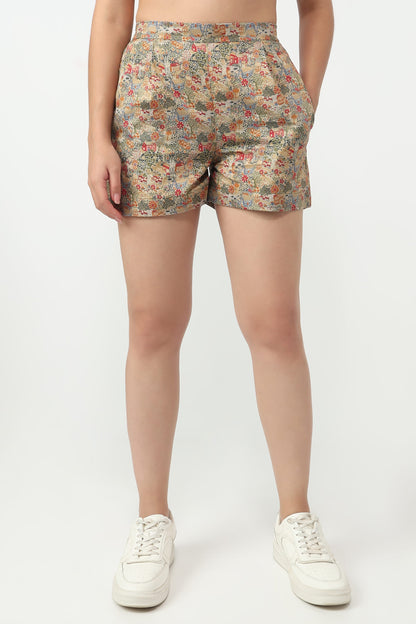 A model from the waist down wearing high-waisted shorts with a dense multicolor floral print on a beige base, paired with white sneakers, against a plain light gray background.