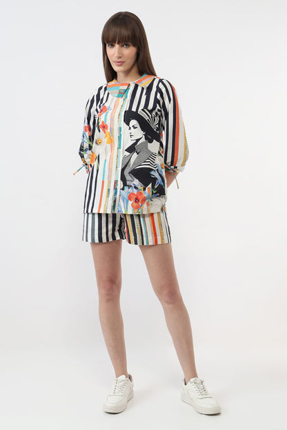 A model wearing a matching two-piece set consisting of a long-sleeve top and shorts. The set features a black and white vertical stripe base with a colorful graphic print of a woman's portrait and floral accents.