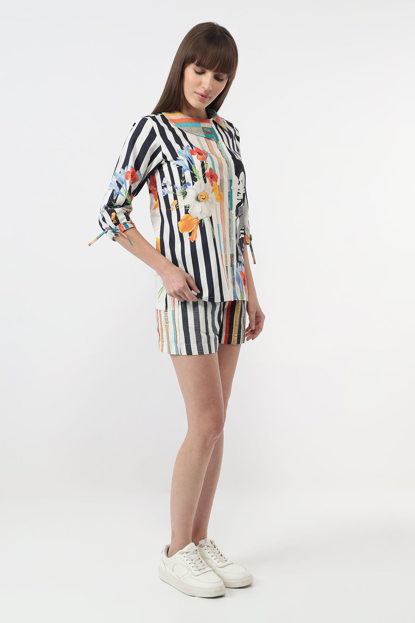 A woman modeling a matching two-piece set consisting of a long-sleeve top and shorts. The set features a black and white vertical stripe pattern with colorful abstract floral and bird motifs.