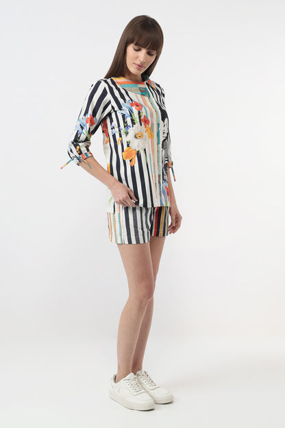 A woman modeling a matching two-piece set consisting of a long-sleeve top and shorts. The set features a black and white vertical stripe pattern with colorful abstract floral and bird motifs.