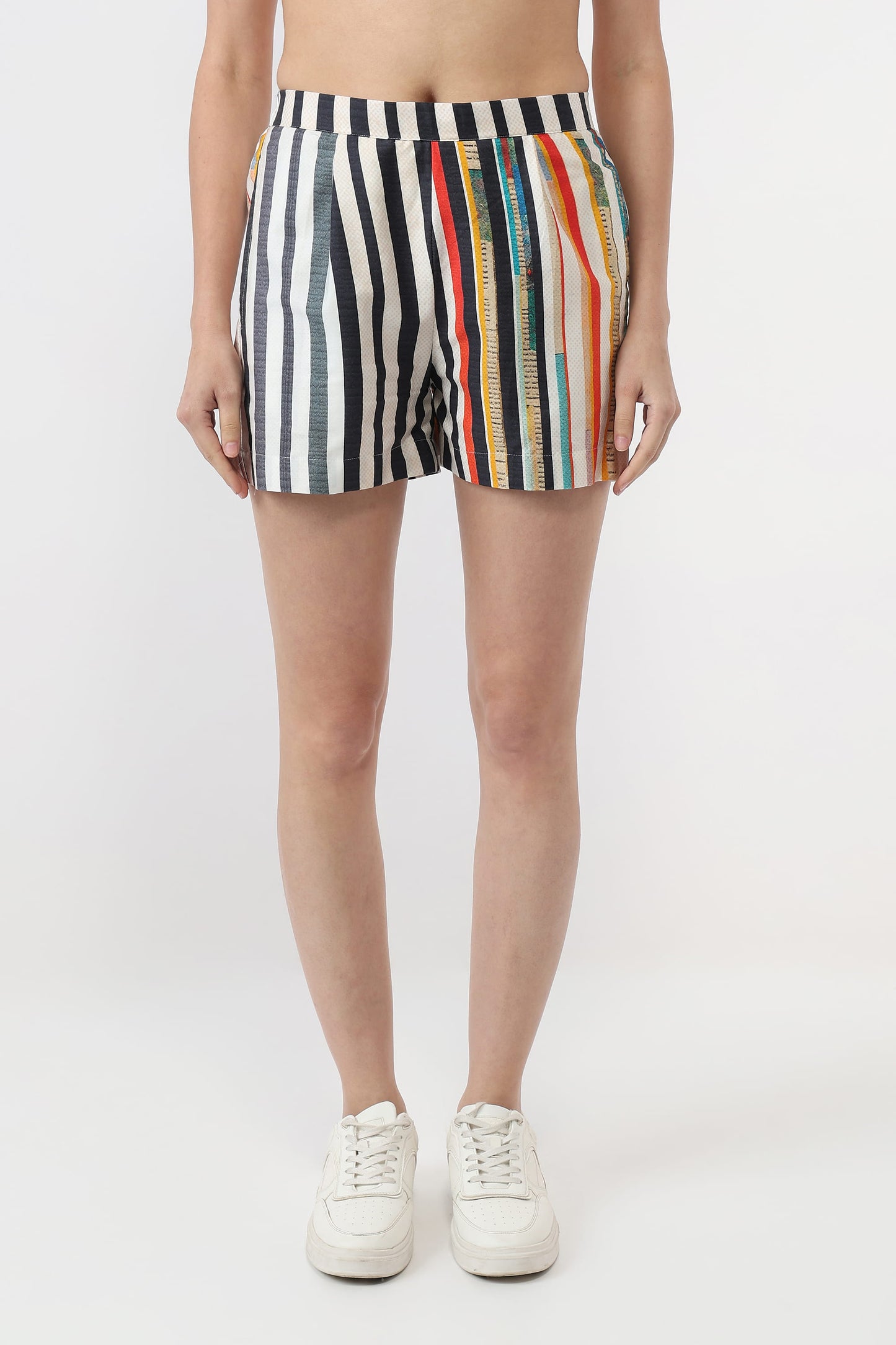 A model from the waist down wearing striped athletic shorts with vertical black, white, and red stripes, along with white sneakers, against a plain white studio background.
