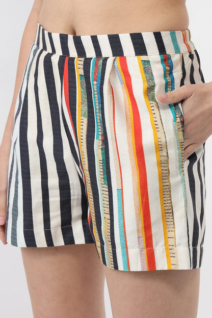 Close-up of a person wearing striped shorts with vertical black, white, red, orange, yellow, and blue stripes, including a side pocket.
