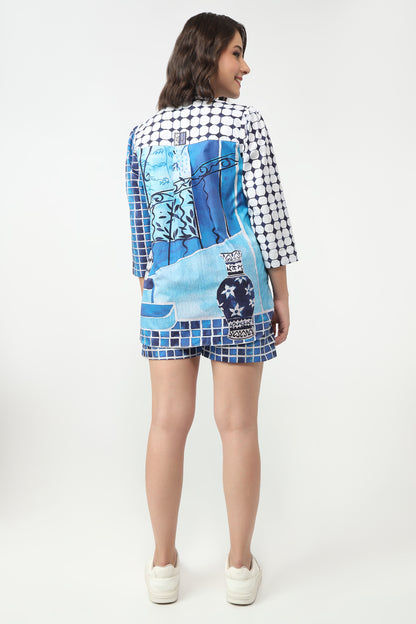 A woman is shown from the back wearing a short-sleeve matching shirt and shorts set. The set features a black and white gingham pattern on the sleeves and collar, with a large blue and white graphic print on the back and front, paired with blue mosaic tile borders.