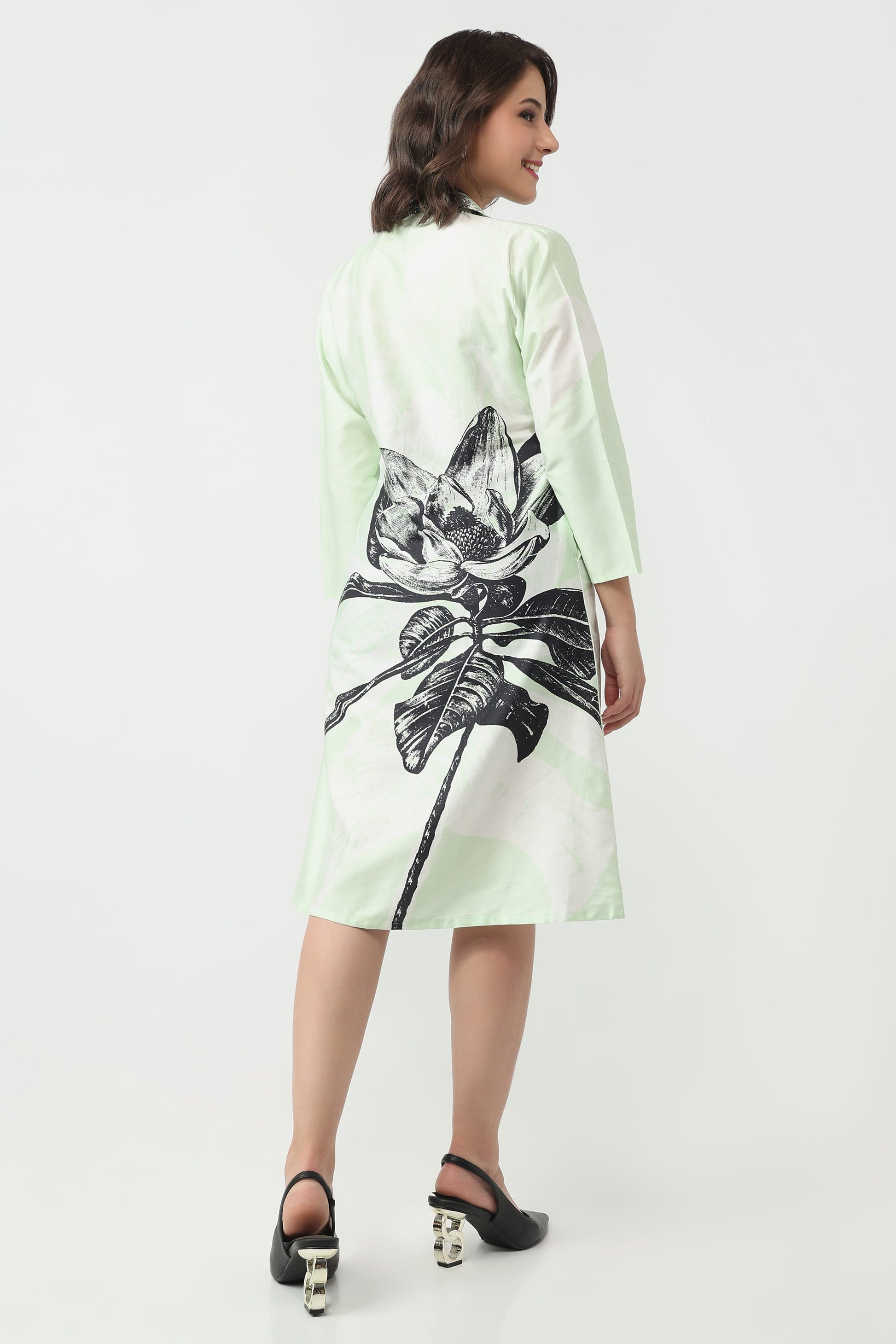 A woman wearing a light mint green and white long-sleeve dress with a large black lotus flower graphic on the back, shown from a three-quarter back view against a plain white studio background.