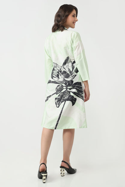 A woman wearing a light mint green and white long-sleeve dress with a large black lotus flower graphic on the back, shown from a three-quarter back view against a plain white studio background.