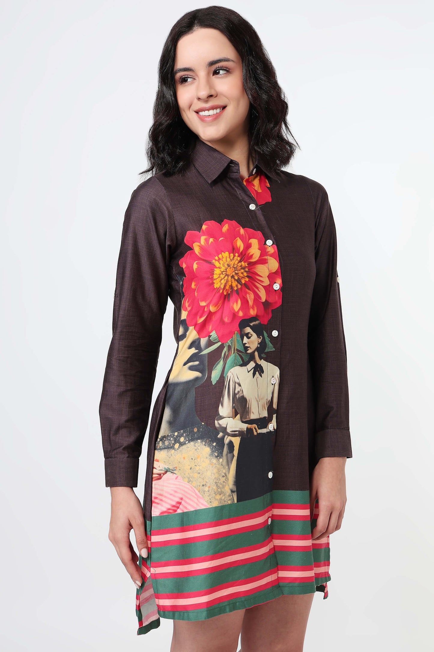 A woman wearing a dark brown long-sleeve shirt dress with a large red and yellow flower print on the back and green and red horizontal stripes on the bottom, paired with black high heels against a white studio background.