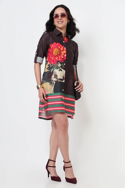 A woman wearing a dark brown long-sleeve shirt dress with a large red and yellow flower print on the back and green and red horizontal stripes on the bottom, paired with black high heels against a white studio background.