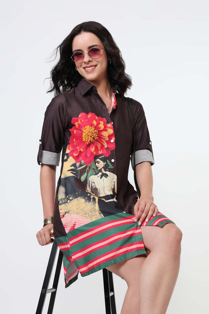 A woman wearing a dark brown long-sleeve shirt dress with a large red and yellow flower print on the back and green and red horizontal stripes on the bottom, paired with black high heels against a white studio background.