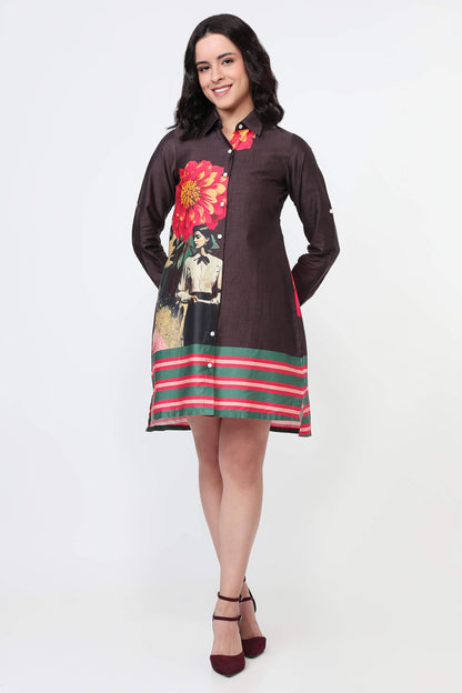 A woman modeling a dark brown long-sleeve shirt dress with a colorful floral and portrait print on the front, a red and green striped hem, and a red floral collar detail, set against a plain white studio background.