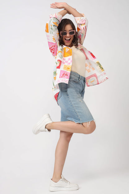 A woman posing in a studio wearing a colorful patchwork print jacket, a light blue denim mini skirt, a beige top, and white sneakers against a light gray background.