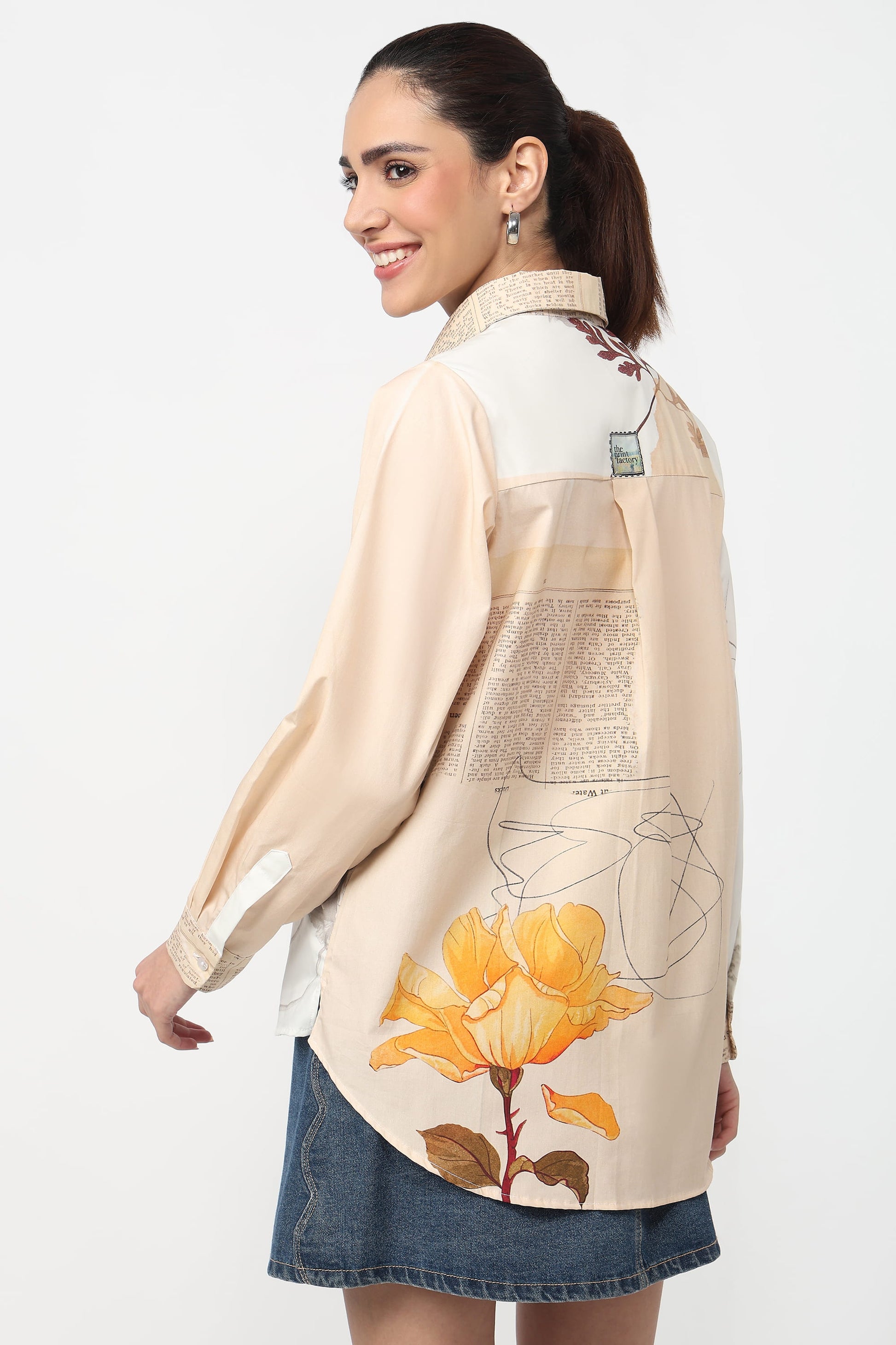 Woman wearing a beige blouse with floral design and denim skirt on a white background