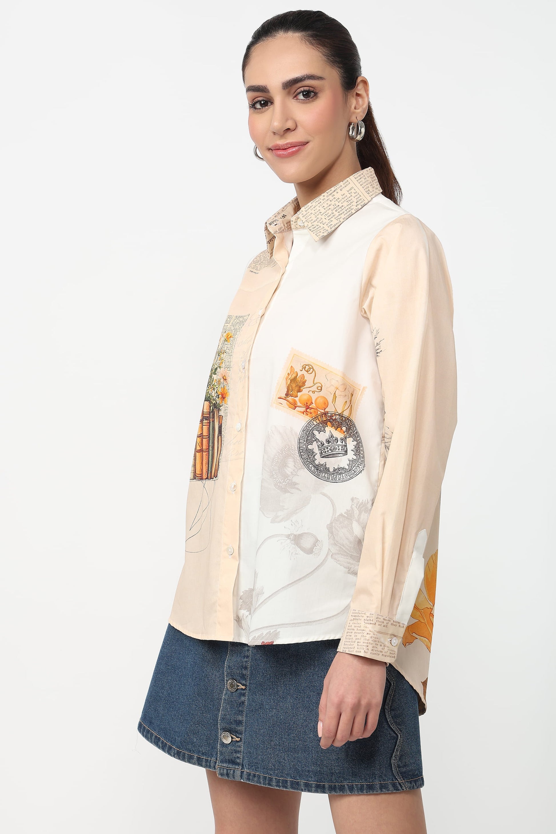 Woman wearing a cream shirt with a graphic design and a denim skirt on a white background