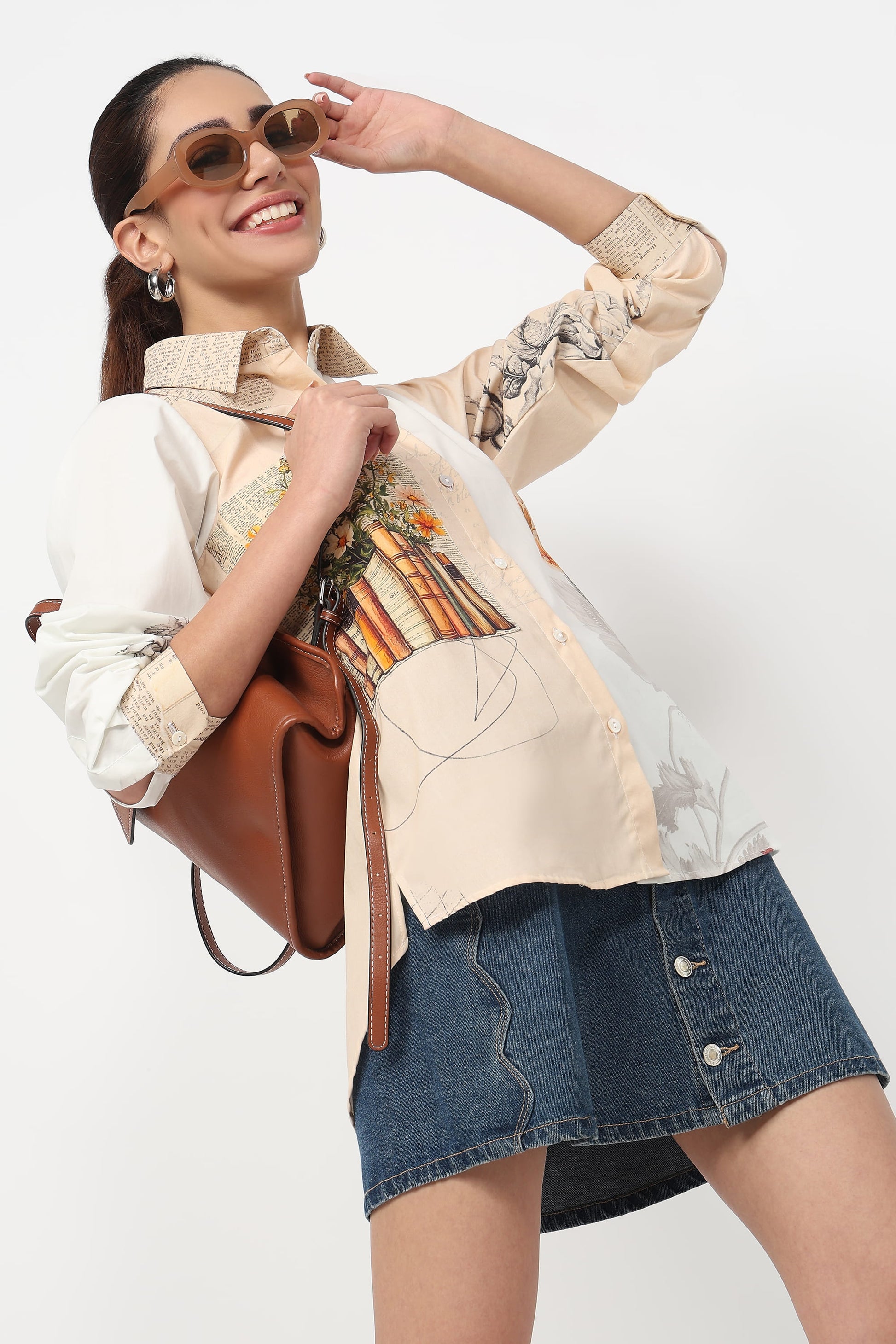 Woman wearing a patterned blouse and denim skirt with a brown handbag on a white background