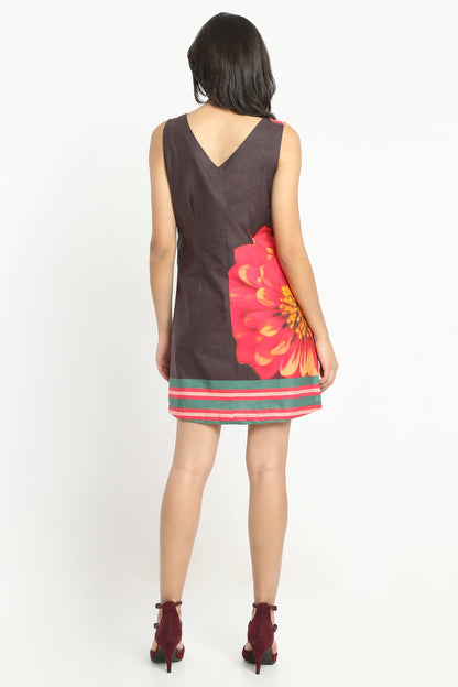 A woman shown from the back wearing a sleeveless dark brown dress with a large red and orange floral print on the back and a striped hem, paired with dark red ankle boots, against a plain white background.