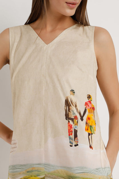 A woman wearing a sleeveless cream-colored mini dress with a colourful illustration of figures on the front and a scenic landscape print along the hem, paired with tan wedge sandals against a plain light white background.
